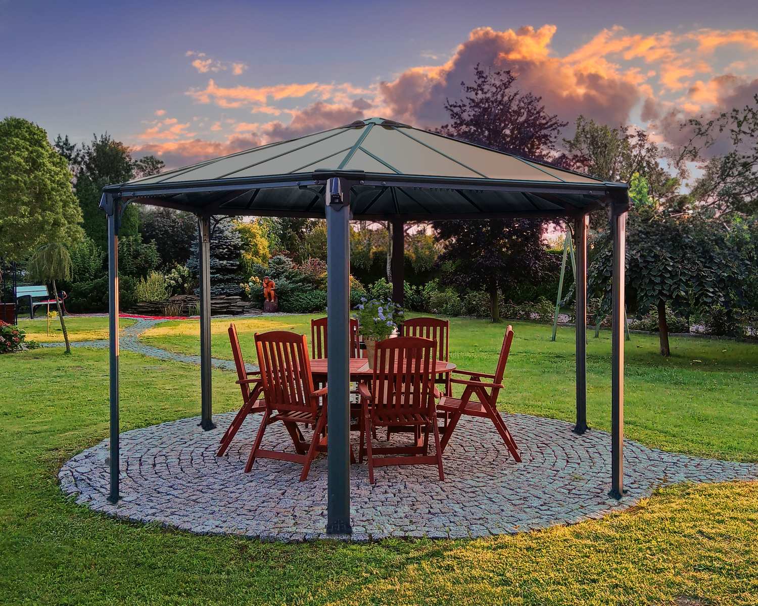 Monaco 13ft x 15ft grey hexagonal aluminum gazebo with wooden table and chairs on a paved patio, set in a lush garden at sunset