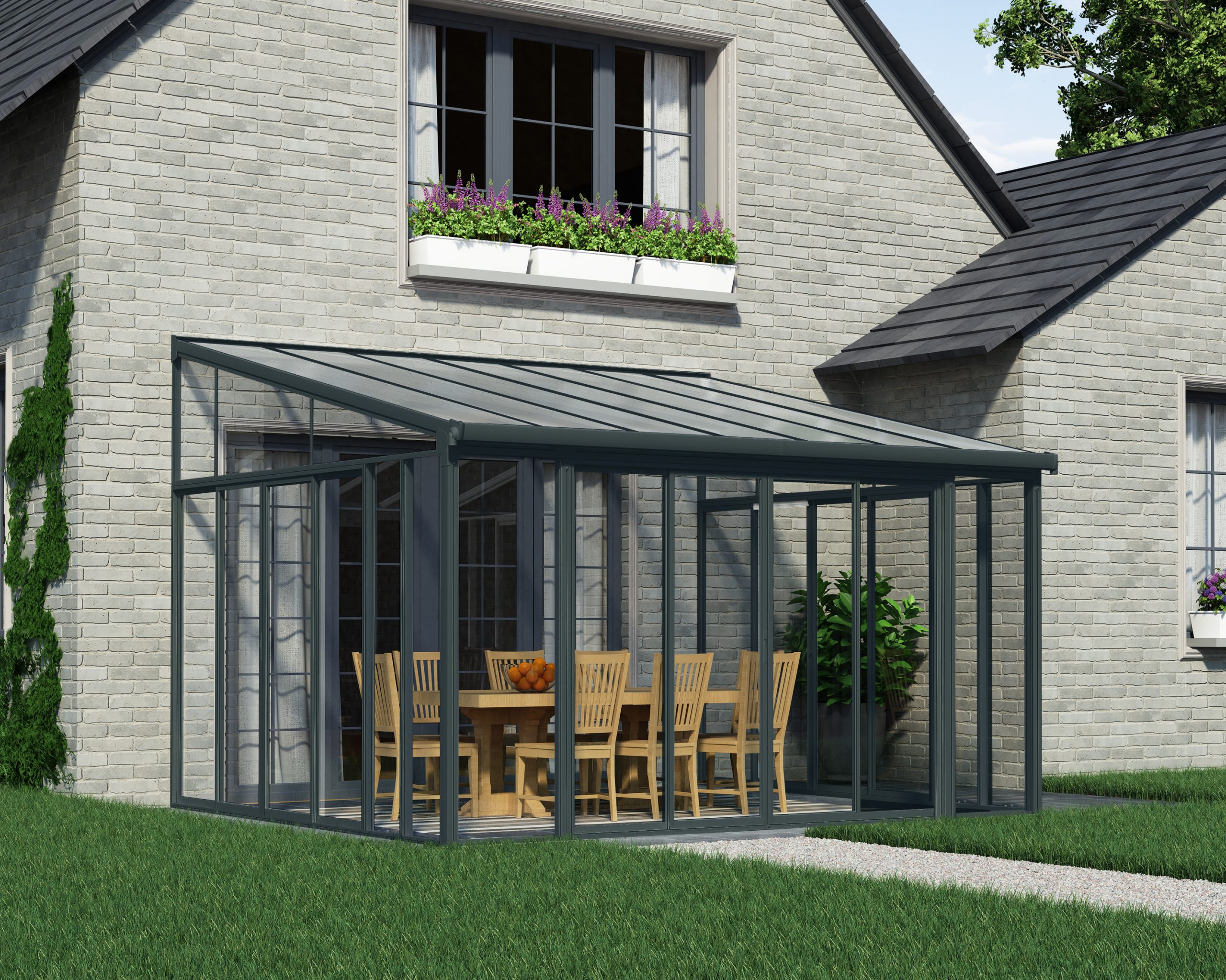 Sanremo grey enclosed gazebo with a clear panel, 13 x 14 ft, with wooden chairs and table, next to a brick house with greenery