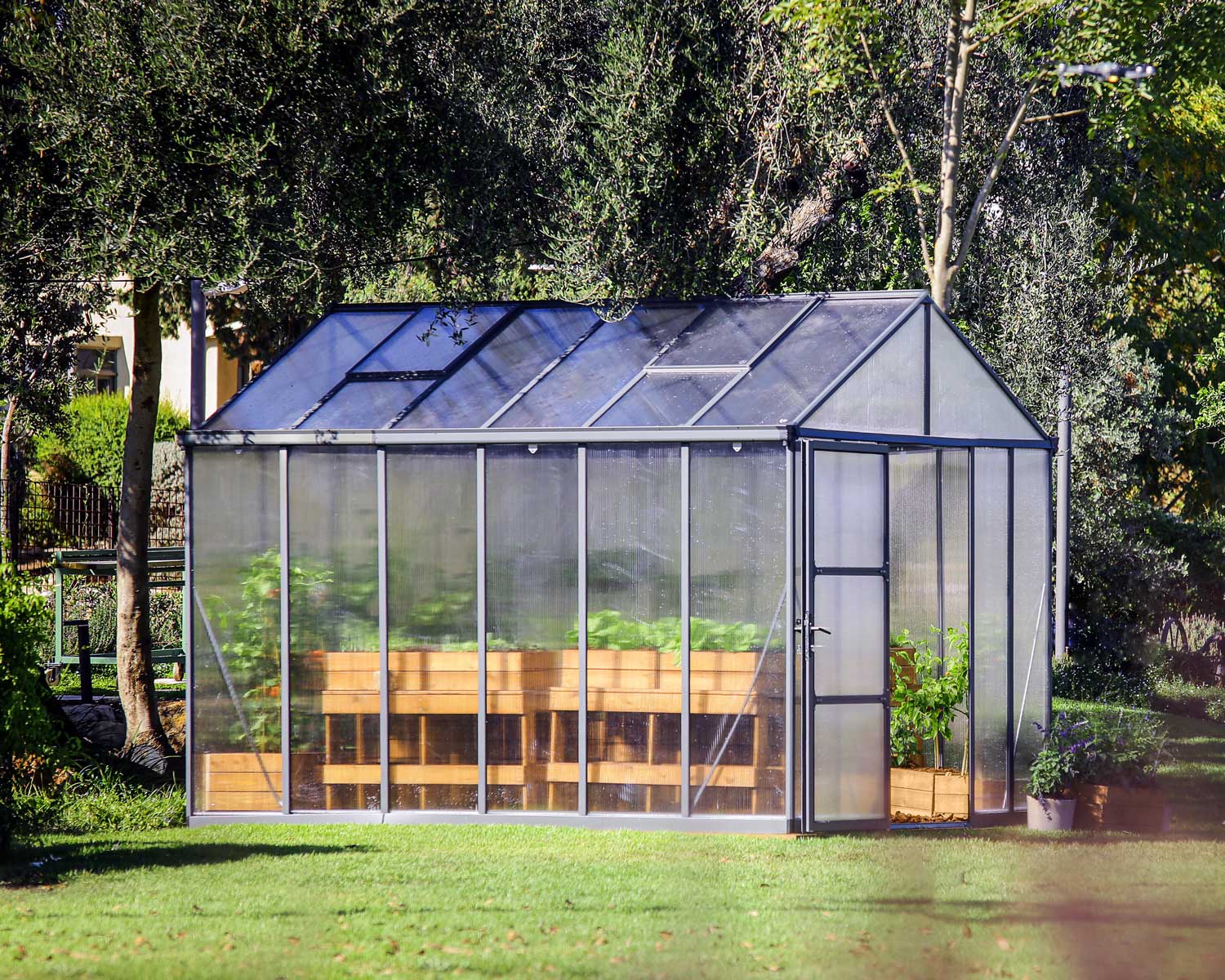 Glory 8ft x 12ft greenhouse featuring a grey frame, multi-wall polycarbonate panels, and vibrant plants inside, nestled in a garden setting