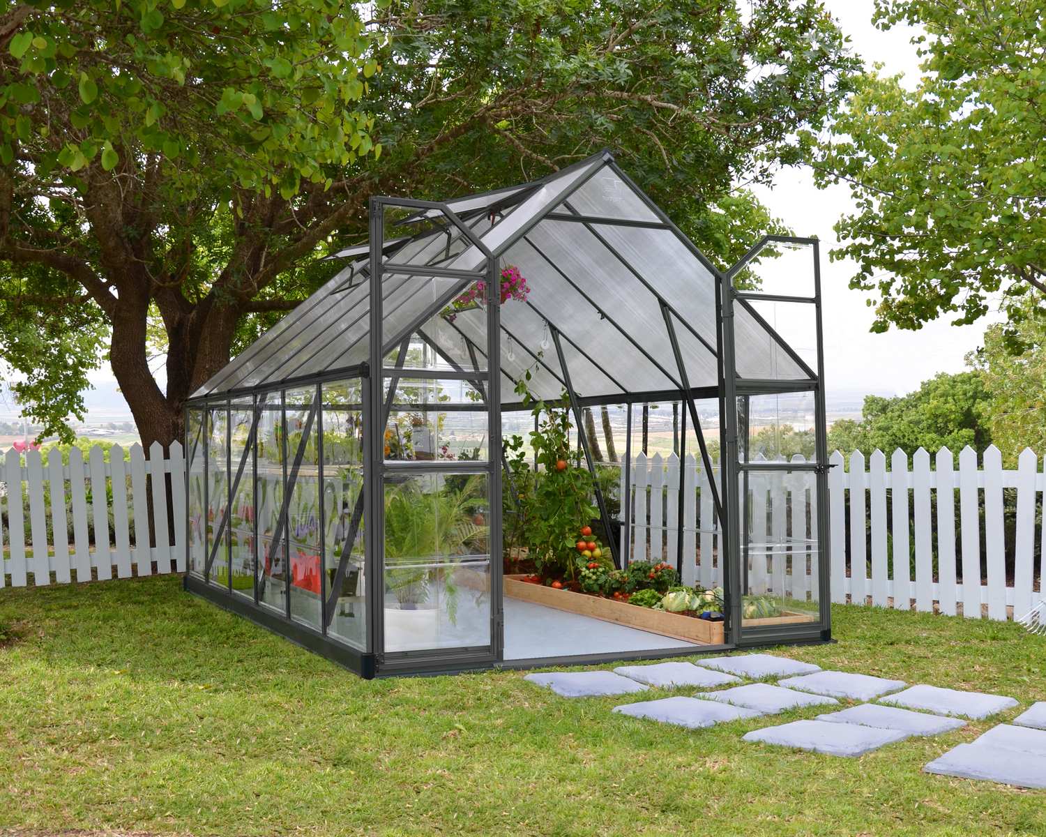 Balance 8ft x 12ft grey greenhouse with clear polycarbonate panels and aluminium frame, on a wet patio, surrounded by a grassy yard and fence