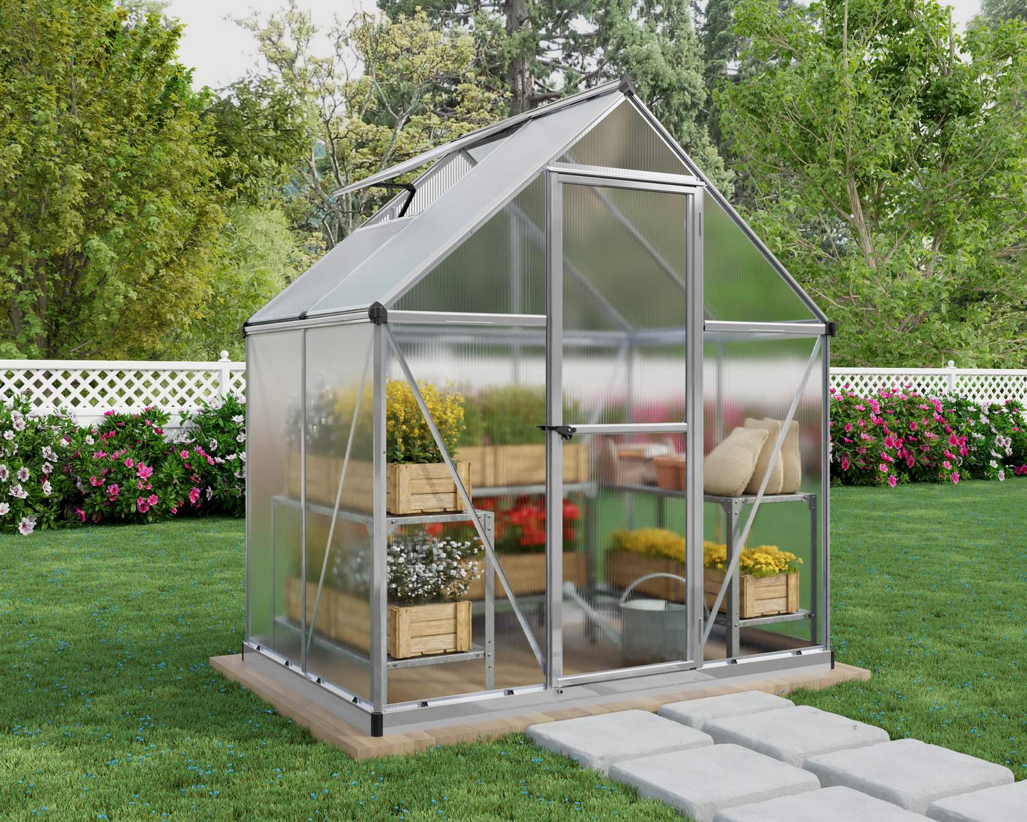 6ft x 4ft silver Mythos greenhouse with aluminum frame and clear polycarbonate panels, in a sunny garden with plants and a white fence