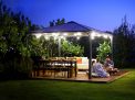 Palermo 12ft x 12ft grey aluminum gazebo with curtains, a sofa with colorful cushions, and a wooden deck in a green garden