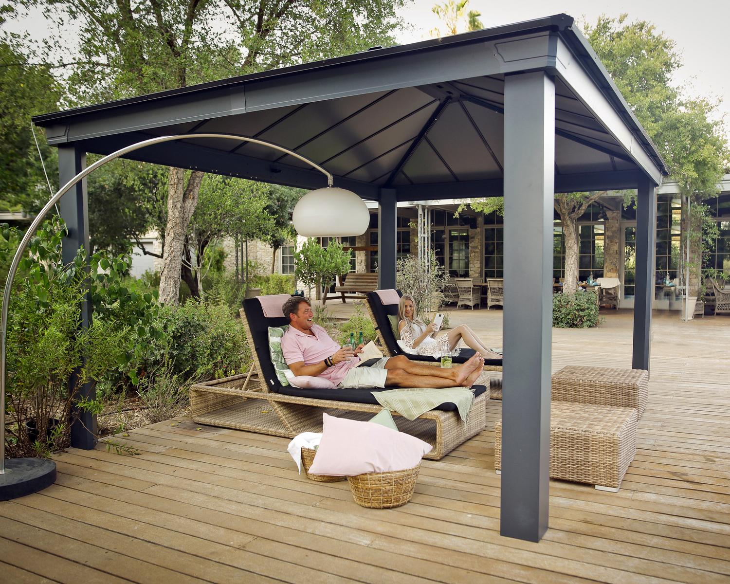 Dallas 12ft x 16ft Grey Twinwall Aluminum Gazebo with HeatBlock technology, featuring seating in a lush garden