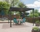 On a garden deck, a dark gray metal gazebo with a flat polycarbonate roof and a couple eating on dining furniture