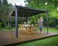 A flat roof gazebo 10&#039; x 14&#039; covers a deck patio with dining furniture and a lady talking on the phone