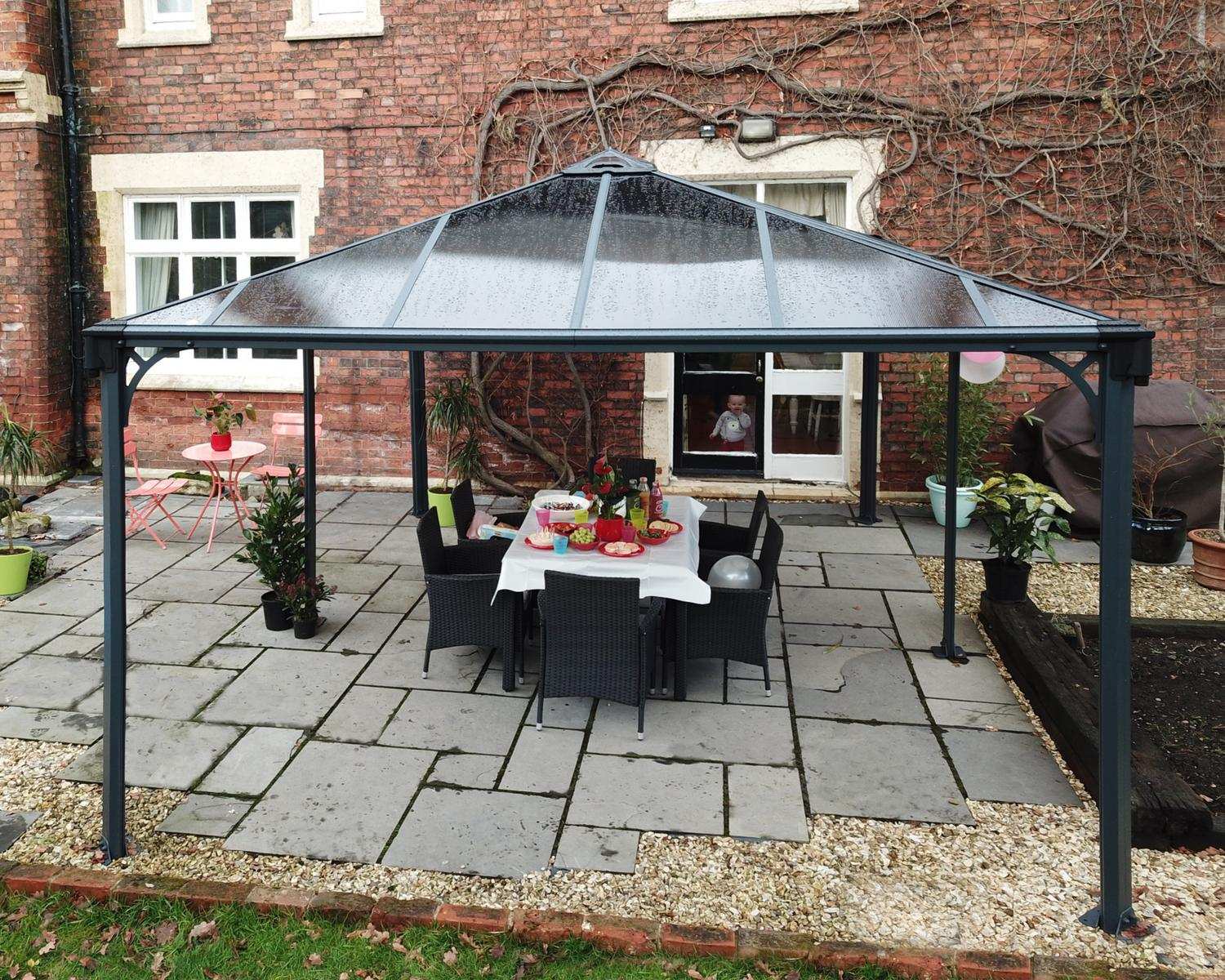 Martinique 12ft x 16ft grey aluminum gazebo with a sleek design, set in front of a brick house for a stylish outdoor retreat.