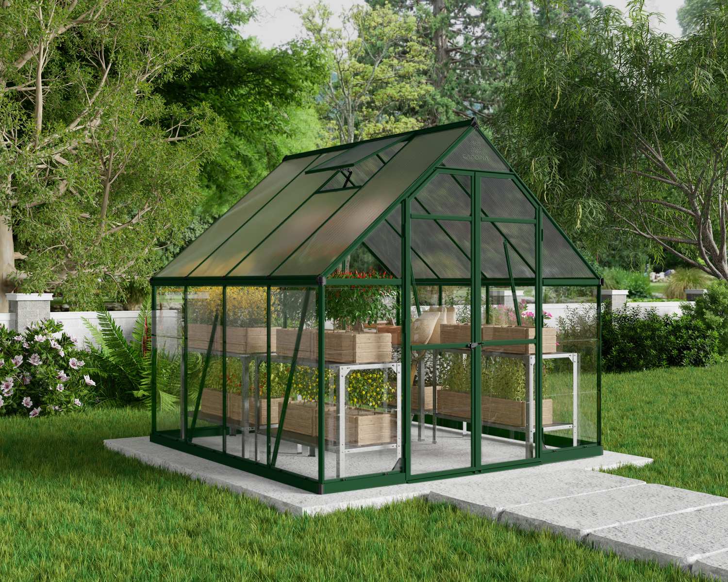 8ft x 8ft green Balance greenhouse with polycarbonate panels and aluminium frame, brimming with plants, beside a white picket fence and shaded by a tree