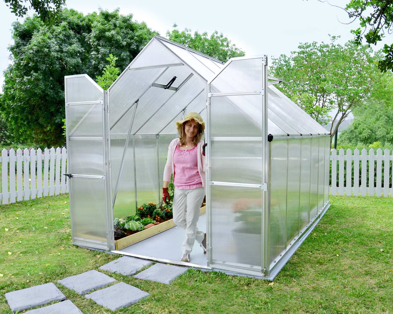 Essence 8x12 Silver greenhouse with polycarbonate panels, double doors, and a sloped roof, set in a vibrant garden