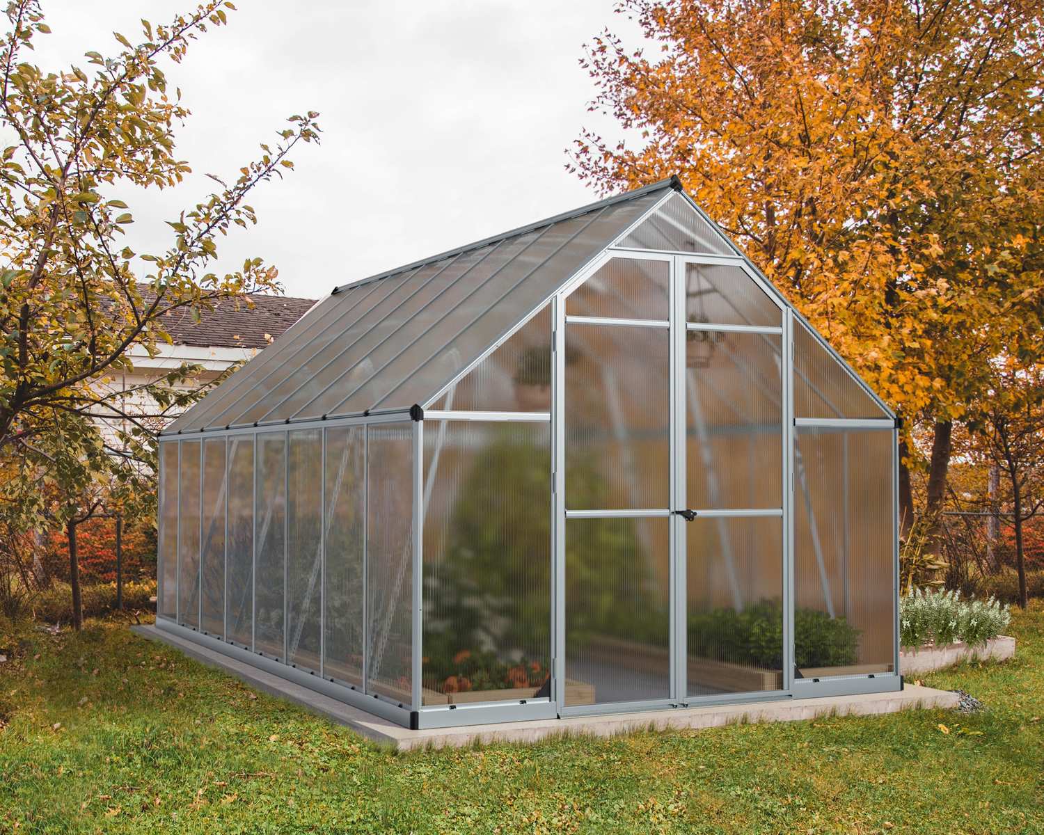 Essence 8x16 Silver greenhouse with polycarbonate panels, double doors, and a sloped roof, set amidst autumn trees