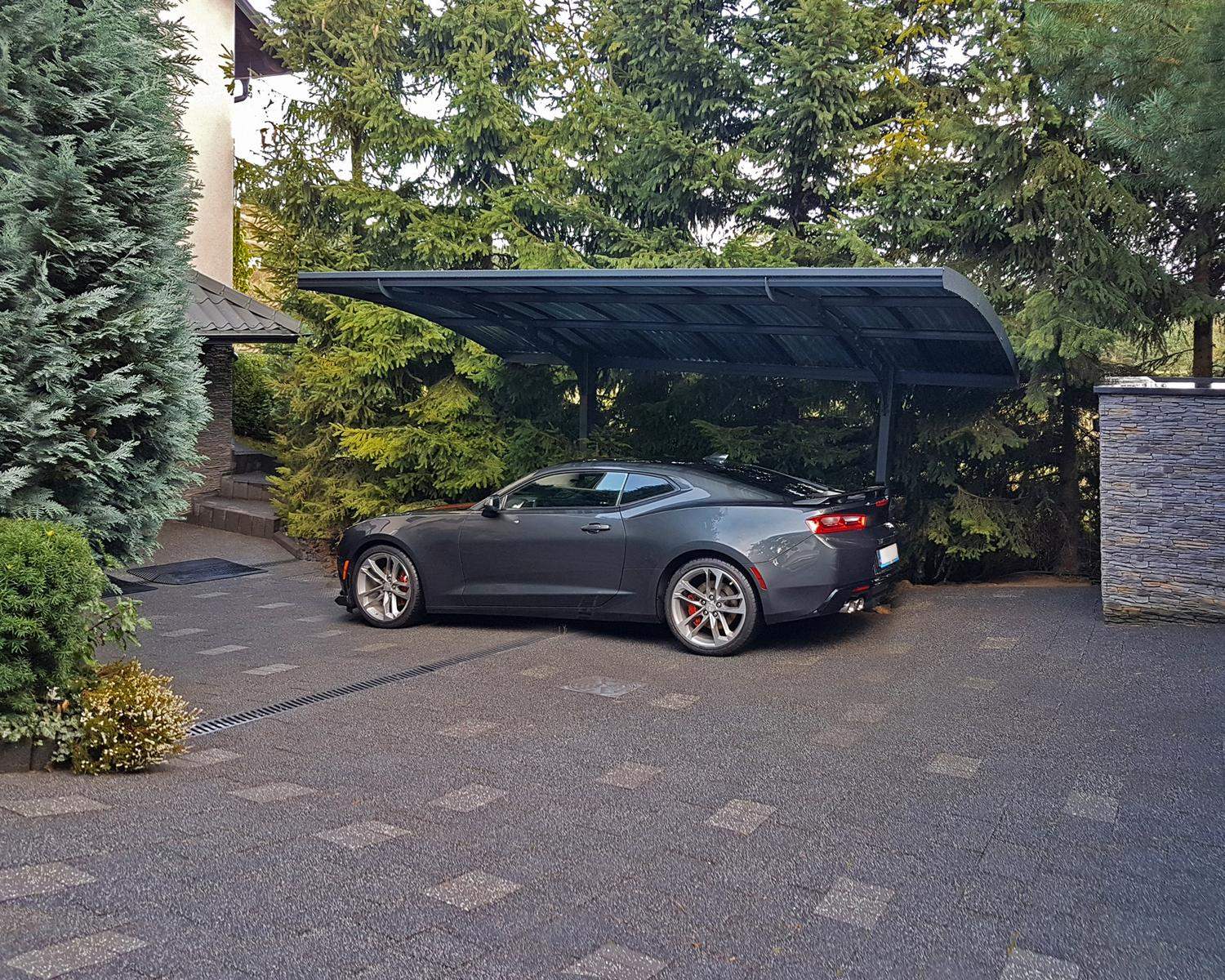 10ft x 16ft Arizona Wave carport with a grey aluminum frame and polycarbonate roof panels, sheltering a sports car next to lush green shrubbery