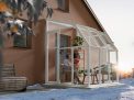 2m x 2m white Lean to Conservatory sunroom with clear polycarbonate panels, featuring a person reading inside, surrounded by snow, with a stunning sunset
