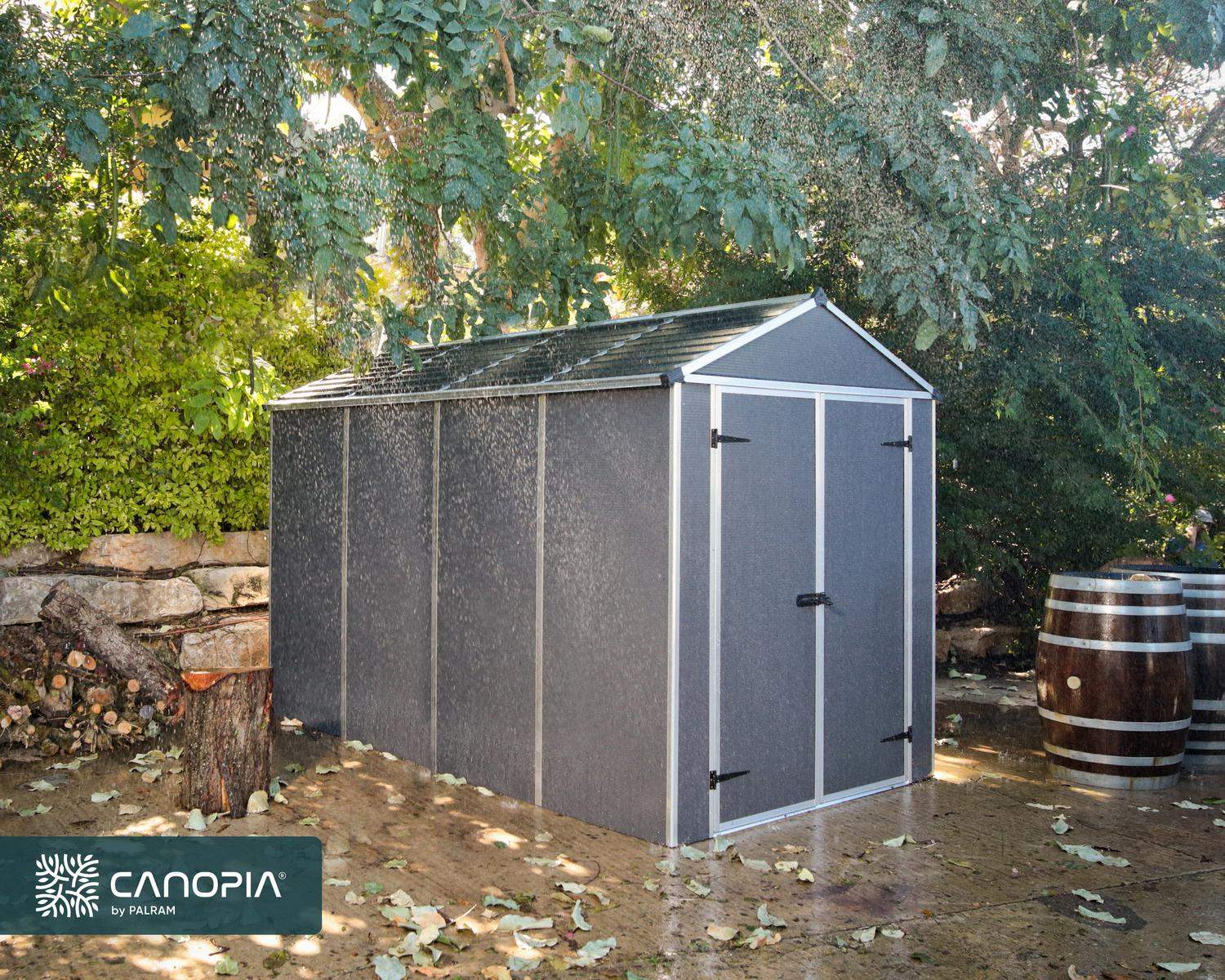 6ft x 10ft grey Rubicon garden shed with a sturdy aluminum frame and multiwall polycarbonate panels, surrounded by greenery and a wooden barrel