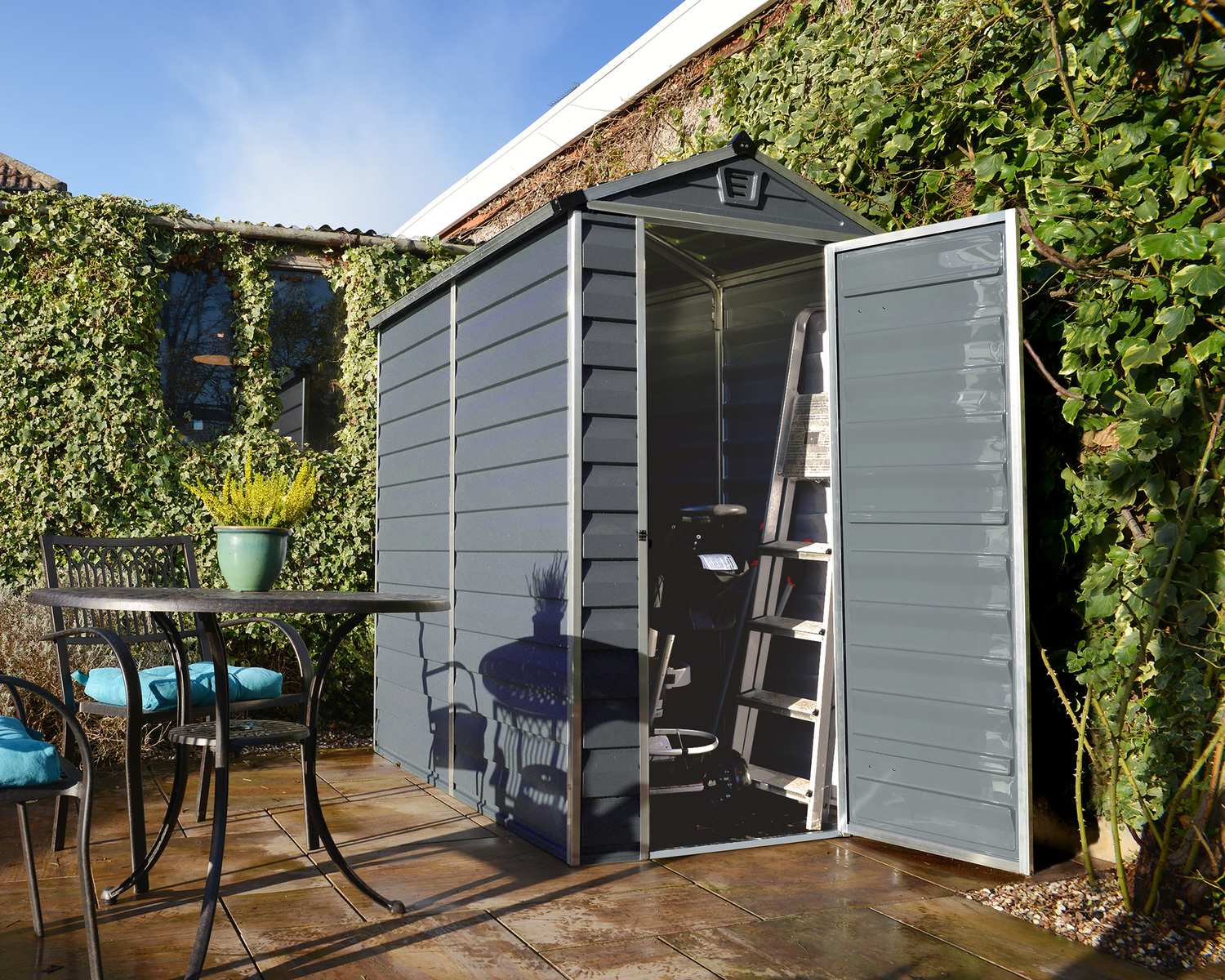 Grey 4ft x 6ft Skylight garden shed with a durable aluminum frame and polycarbonate panels, placed on a concrete base amidst greenery