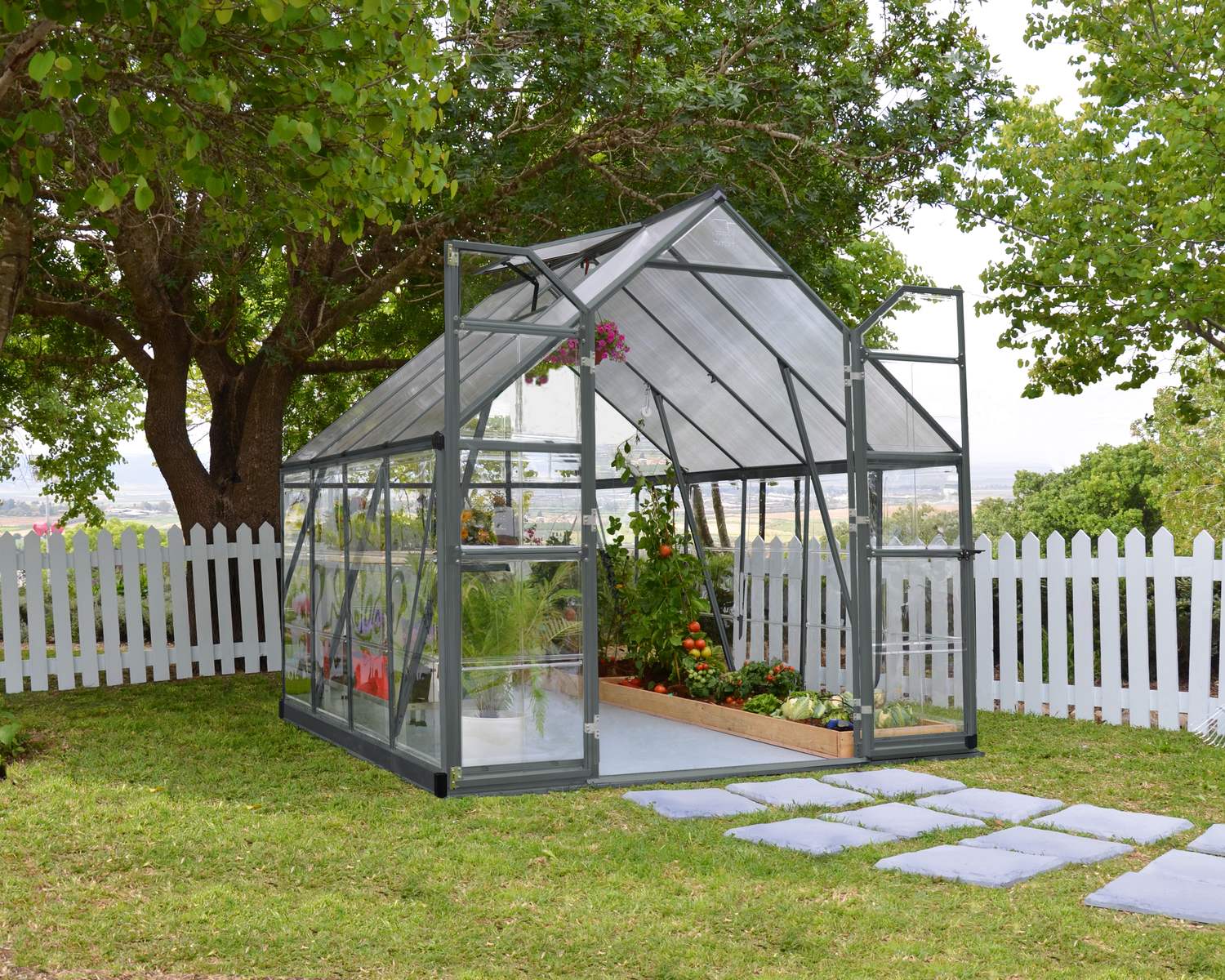 8ft x 8ft grey Balance greenhouse with an aluminum frame and clear polycarbonate panels, set in a garden with vibrant greenery