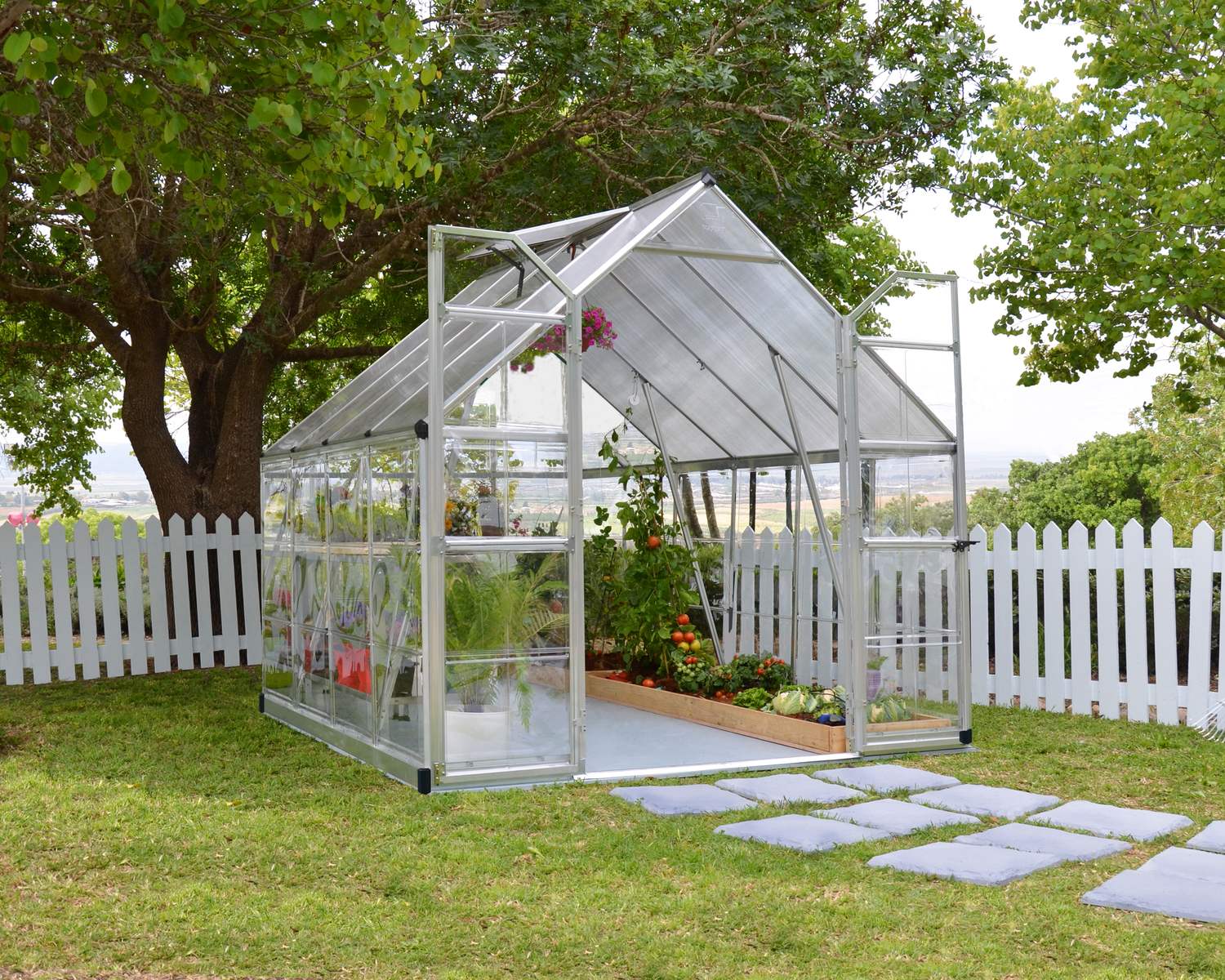 8ft x 8ft silver Balance greenhouse with an aluminum frame, clear polycarbonate panels, and plants, set in a garden with trees