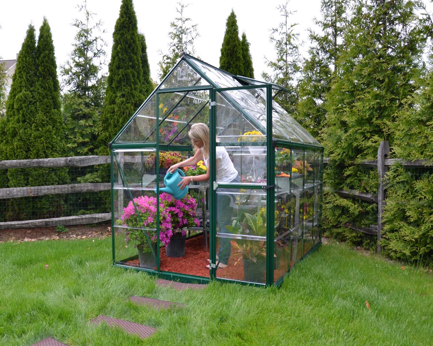 6ft x 8ft green Harmony greenhouse with clear polycarbonate panels and an aluminum frame, set on a residential patio near a beige house