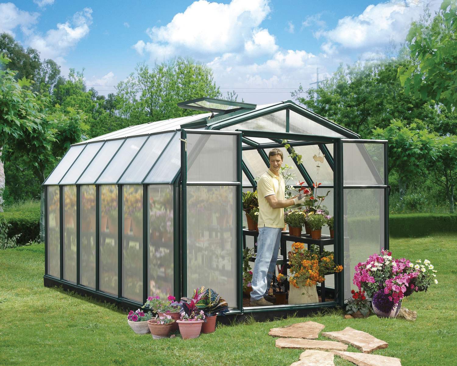 8ft x 12ft green Hobby Gardener greenhouse with aluminum framing and twin-wall polycarbonate panels, surrounded by plants and gardening tools
