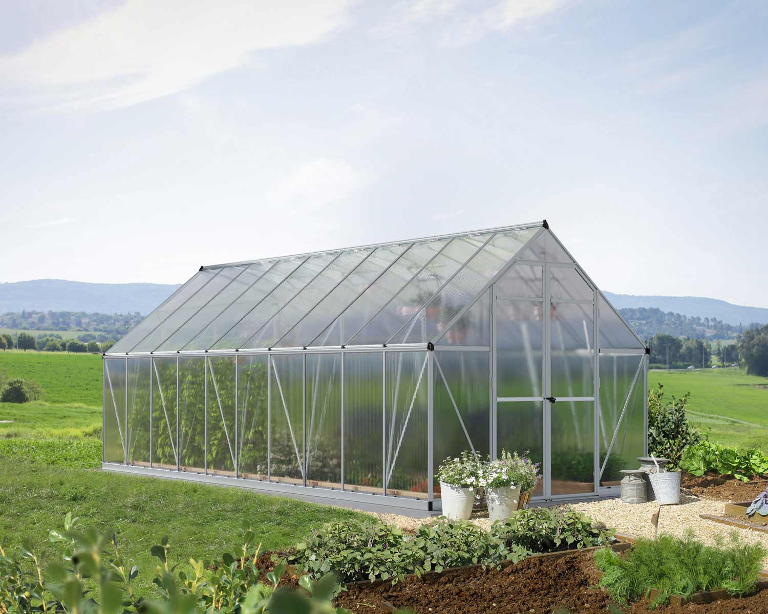 8ft x 20ft silver Essence greenhouse with an aluminum frame and multi-wall polycarbonate panels, set in a lush garden