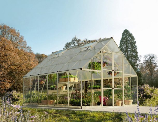 10ft x 12ft silver Balance greenhouse with aluminum frame and clear polycarbonate panels, brimming with plants and surrounded by lush greenery