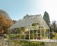 10ft x 12ft silver Balance greenhouse with aluminum frame and clear polycarbonate panels, brimming with plants and surrounded by lush greenery