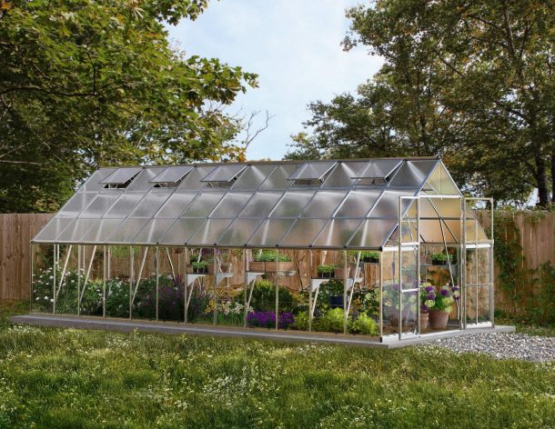 10ft x 24ft silver Balance greenhouse with an aluminum frame, clear polycarbonate panels, filled with plants, in a backyard with a wooden fence