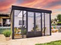 Stylish Copenhagen 3m x 3.5m black enclosed gazebo with an aluminum frame and clear polycarbonate panels, set in a serene garden at sunset