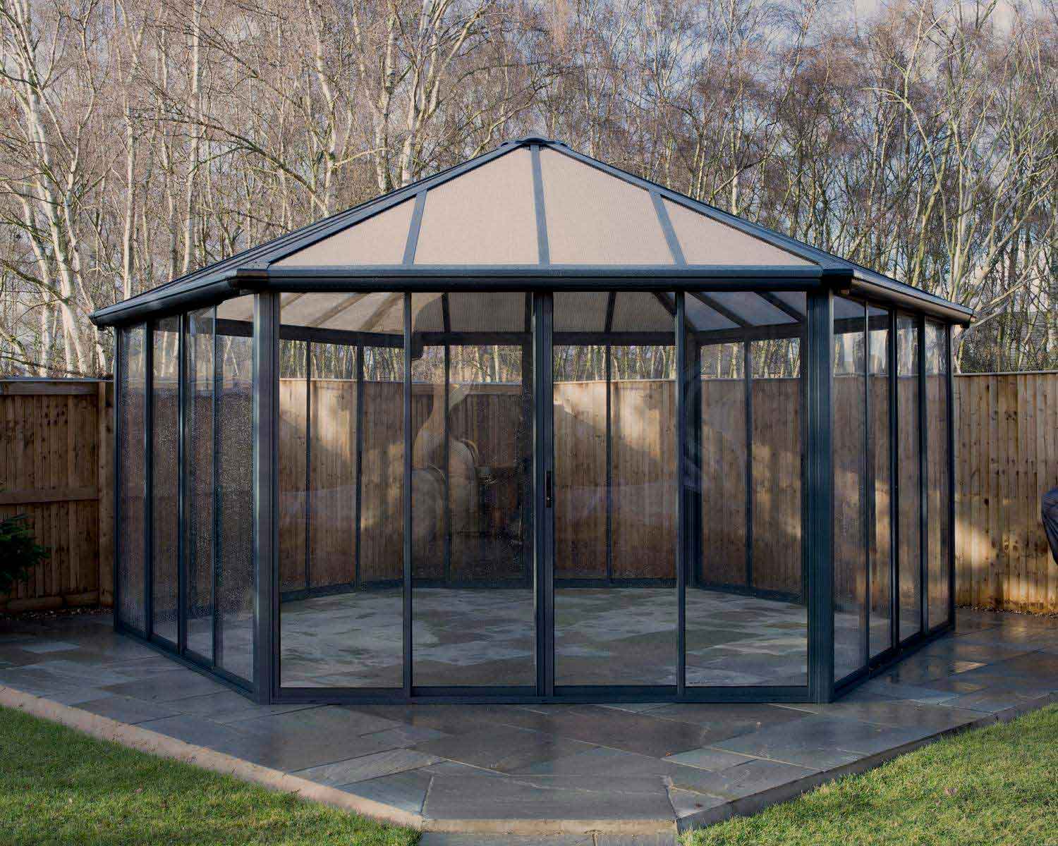Modern grey Garda 6m x 5m enclosed gazebo with polycarbonate panels and sturdy frame, featuring outdoor setting