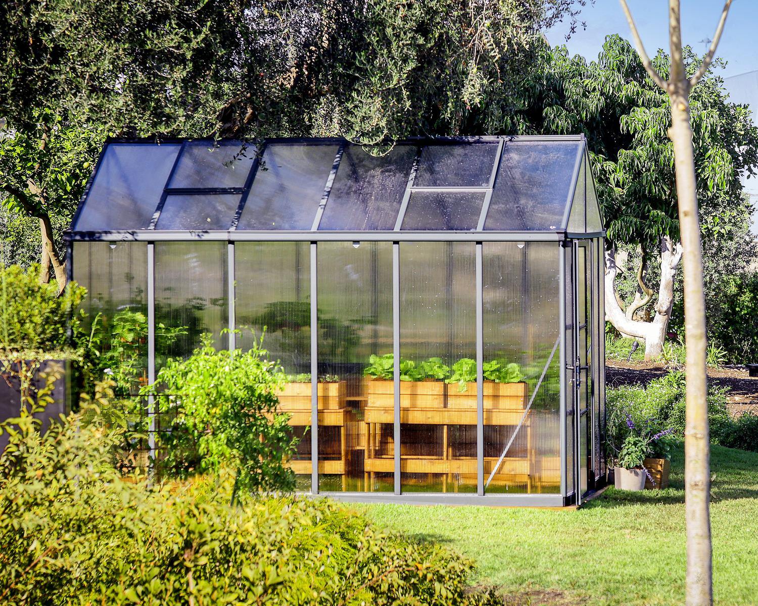 8ft x 12ft grey Glory greenhouse with an aluminum frame and multi-wall polycarbonate panels, surrounded by greenery