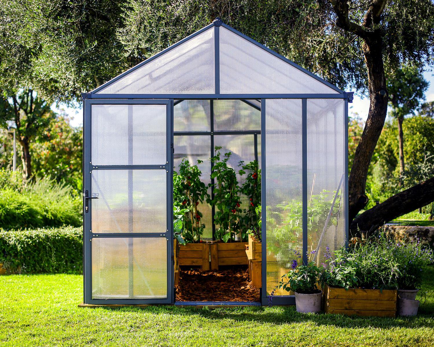 8ft x 12ft grey Glory greenhouse with an aluminum frame and multi-wall polycarbonate panels, surrounded by greenery
