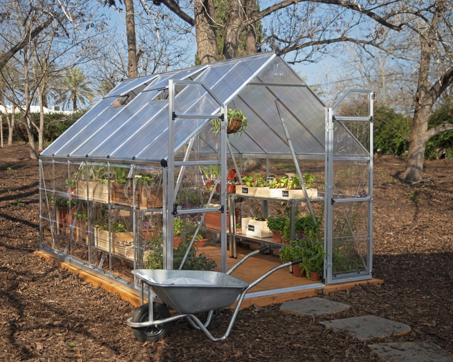 8ft x 12ft silver Balance greenhouse with a sturdy aluminum frame and clear polycarbonate panels, nestled in a garden with a stone pathway