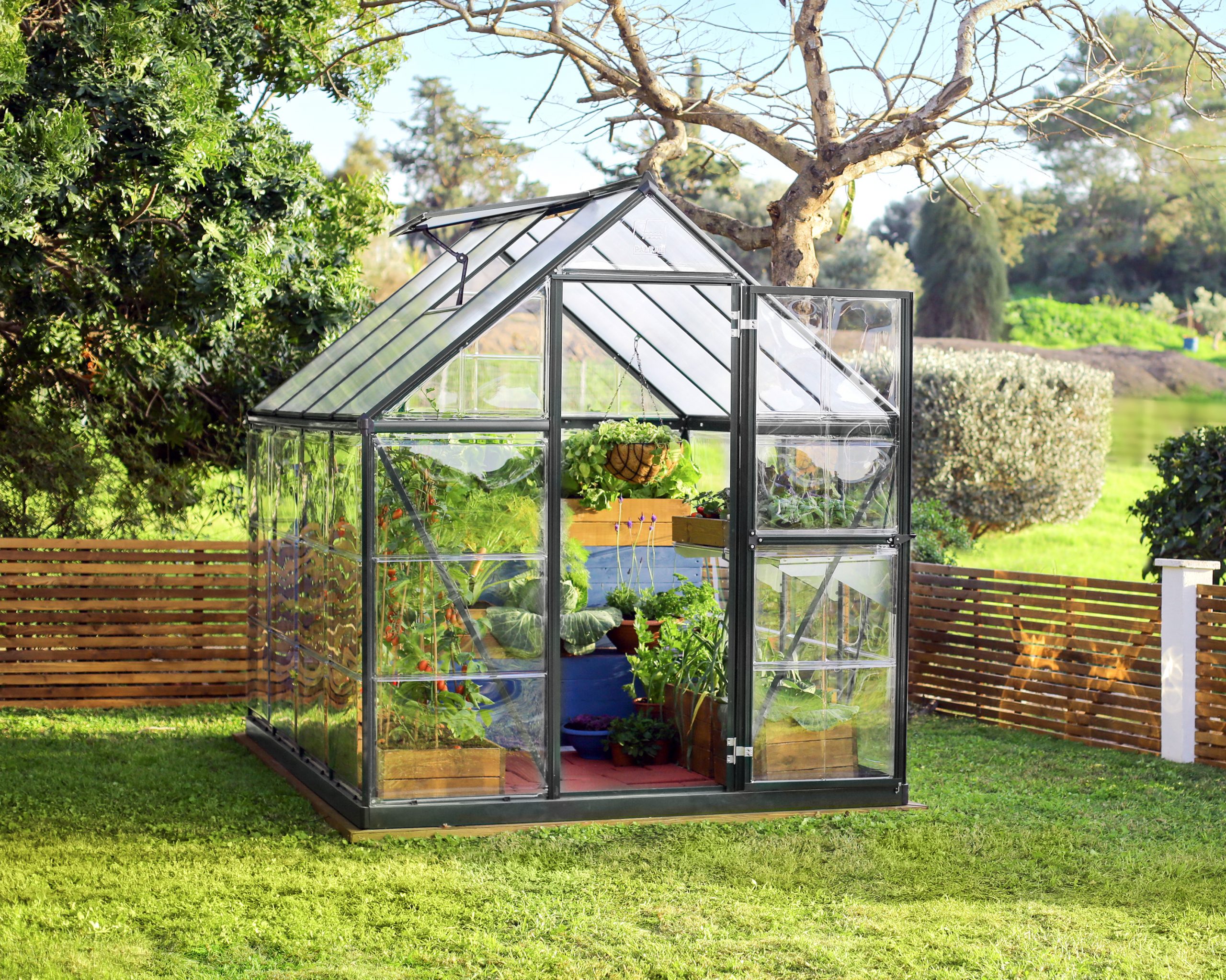 6ft x 8ft grey Hybrid greenhouse with an aluminum frame and clear polycarbonate panels, tucked away in a vibrant garden