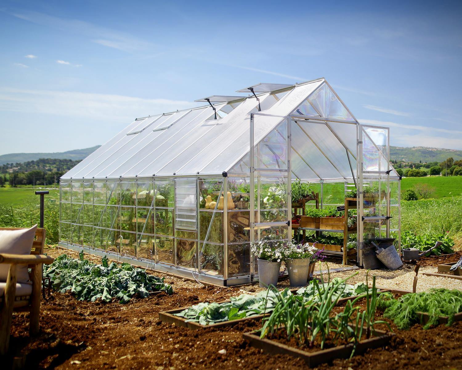 10ft x 20ft silver Balance greenhouse with an aluminum frame and clear polycarbonate panels, filled with plants in a garden setting