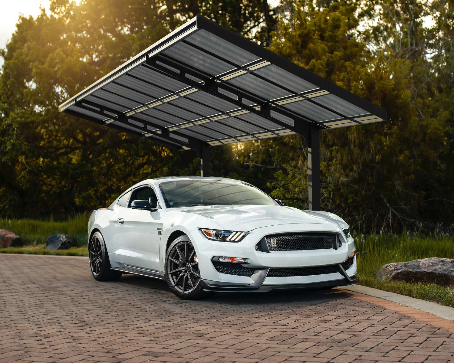 10ft x 20ft Sydney Wave carport with a black aluminum frame and polycarbonate roof, sheltering a white sports car in greenery